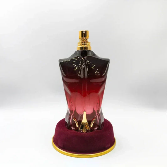Perfume bottle shaped like a torso on a red stand with gold accents against a white background