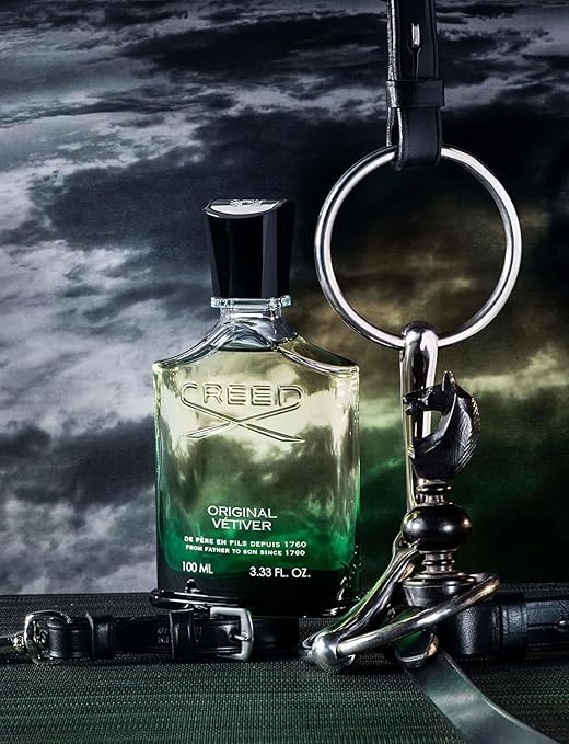 Creed Original Vetiver perfume bottle with keychain and belt on a dark background