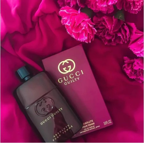 Gucci Guilty Absolute Pour Femme perfume bottle and packaging on a pink background with flowers.