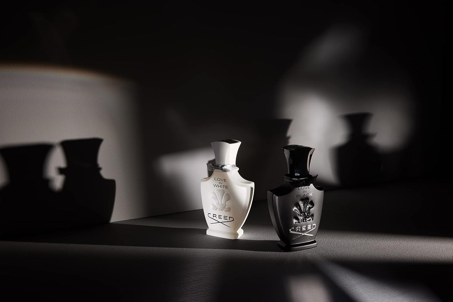 Two Creed perfume bottles on a dark surface with soft focus background