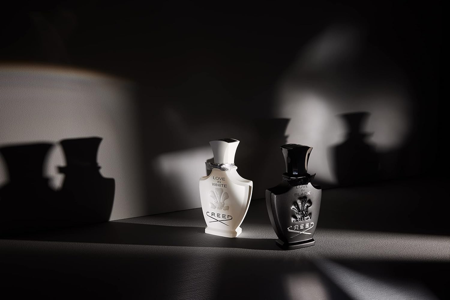 Two Creed perfume bottles on a dark surface with soft focus background