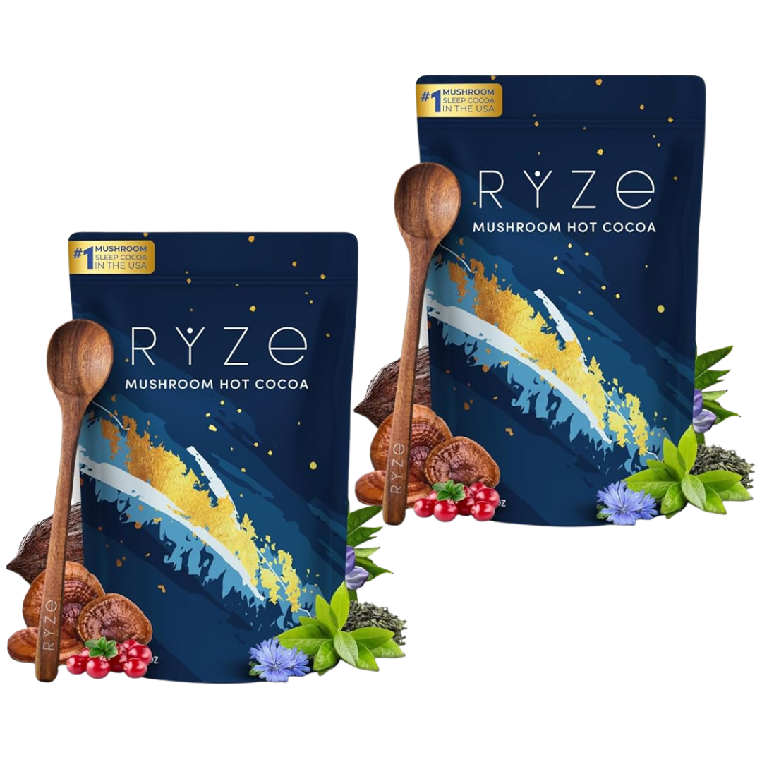 Two bags of RYZE Mushroom Hot Cocoa arranged on a white background, each with a wooden spoon, cocoa pods, berries, and green leaves around the base. The bags are dark blue with white and gold artwork and a small gold badge reading 'Mushroom Hot Cocoa'.